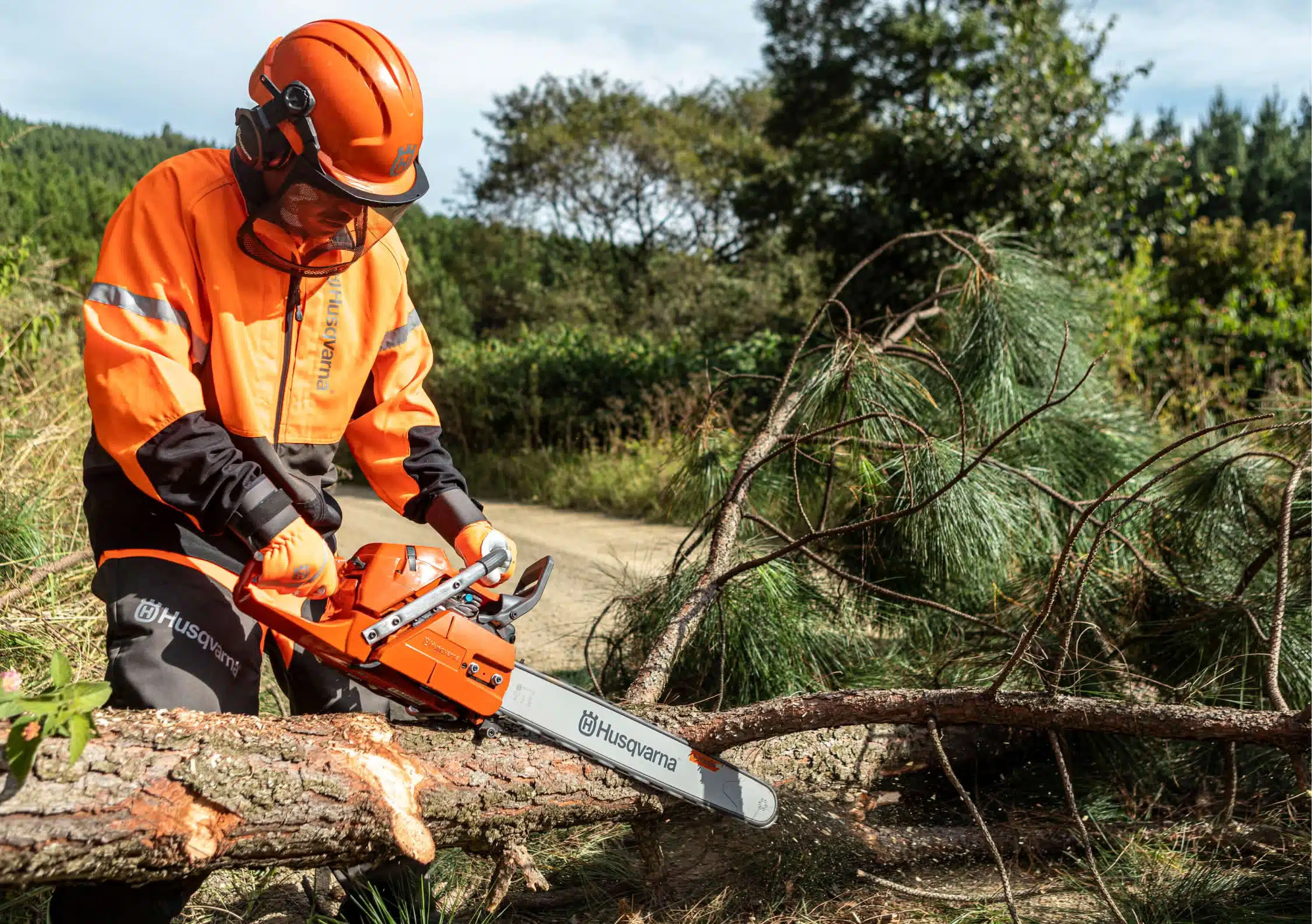 Hombre con equipación de trabajo sujetando una motosierra Husqvarna sobre un árbol caído en un entorno natural