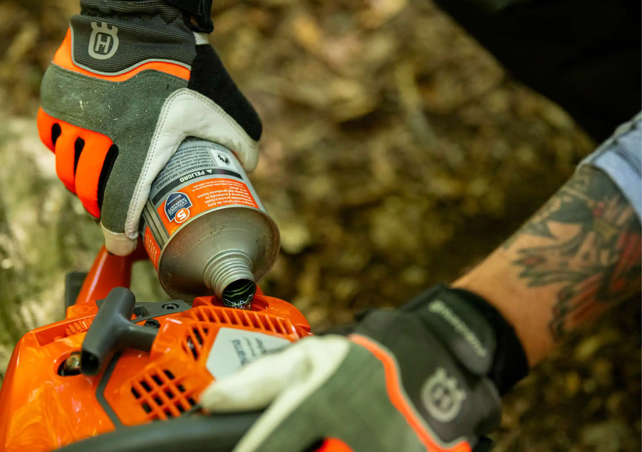Manos con guantes Husqvarna rellenando el depósito de una motosierra